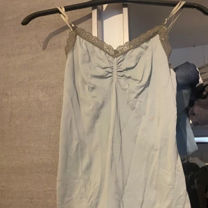 Ljusblå linnetopp med spetsdetaljer - Säljer en ljusgrön/blåaktig linnetopp med tunna axelband och fina spetsdetaljer längs urringningen. Toppen har en rynkad detalj framtill. Perfekt för sommaren!