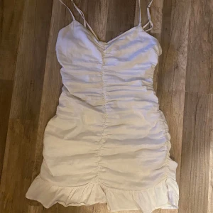 Zara vit omlottklänning med volang - Säljer en söt vit klänning med smala axelband och volangkant nertill. Klänningen har en lätt rynkad effekt framtill och är figurnära med omlottkänsla. Perfekt för sommarens alla tillfällen! Xs-s