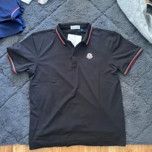Svart pikétröja från Moncler - Säljer en svart pikétröja från Moncler med klassisk krage, helt ny, 999kr