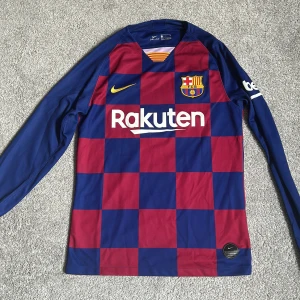 FC Barcelona 19/20 långärmad fotbollströja Messi 10 - Säljer en långärmad FC Barcelona matchtröja från Nike med rutigt mönster i blått och rött. Tröjan har Messi och nummer 10 på ryggen, samt sponsortryck från Rakuten och Unicef. Officiell La Liga-patch på ärmen. Produkten är i princip i perfekt skick förutom väldigt minimal skada på nummer 10 (bild 4). Köparen står för frakt. Medela mig om du har några frågor!