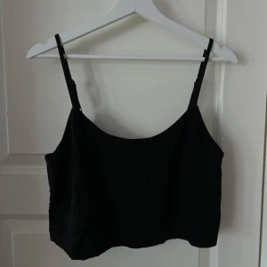 Svart croppad linne - En enkel och stilren svart linnetopp med smala justerbara axelband. Toppen har en rak passform och är croppad, perfekt att matcha med höga jeans eller kjol. Kollektion Lisa&Lena för NA-KD.