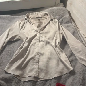 Ljusbeige satinskjorta från H&M - Ljusbeige skjorta från H&M i satinliknande material.