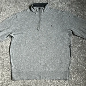 Grå quarter zip tröja från Polo Ralph Lauren - Säljer en stilren grå långärmad tröja från Polo Ralph Lauren. Riktigt bra skick och har bara använts få talet gånger (max 3 stycken). Köparen står för frakt. Hör av dig om du har några frågor!
