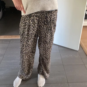 Leopardmönstrade vida byxor med resår - Säljer ett par snygga leopardmönstrade byxor med bred resår i midjan och avslappnad passform. Byxorna är vida i benen och har snörning i midjan för extra komfort. Perfekta för dig som gillar sköna glamourösa kläder!