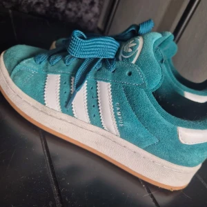  Adidas Campus sneakers - Säljer ett par turkosa Adidas Campus sneakers med vit sula och vita ränder på sidorna. Skorna har snörning och är i mocka med klassisk Adidas-logga på plösen. Perfekta för dig som gillar färg och streetstyle. Köpta för 1700kr