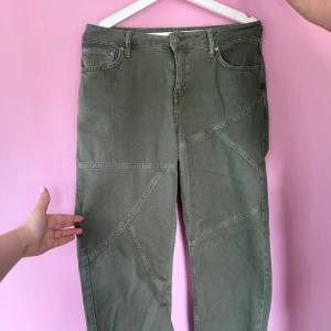 Olivgröna jeansbyxor från NA-KD - Säljer ett par olivgröna jeansbyxor från NA-KD med unika sömdetaljer över benen. Byxorna har klassisk femficksdesign, normal passform och stängs med dragkedja och knapp. Perfekta för dig som vill ha något lite annorlunda i garderoben.