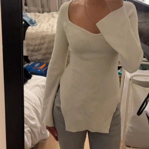 Ribbad vit långärmad topp - Säljer en ribbad vit långärmad topp med v-ringad hals och figurnära passform. Toppen har långa, lätt utsvängda ärmar och är tillverkad i ett stretchigt stickat material som sitter snyggt på kroppen. Perfekt att styla med jeans eller kjol.