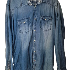 Blå jeansskjorta Jack & Jones XL - Snygg blå jeansskjorta från Jack & Jones i storlek XL. Skjortan har två bröstfickor med lock och tryckknappar, klassisk krage och långa ärmar. Perfekt för dig som gillar avslappnad stil med denimkänsla.