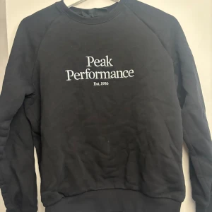 Svart Peak Performance sweatshirt S - Svart sweatshirt från Peak Performance med vit broderad logga på bröstet. Klassisk rund halsringning och långa ärmar. Perfekt för en chill och stilren look. Mjuk insida och ribbade muddar vid ärmslut och nederkant.