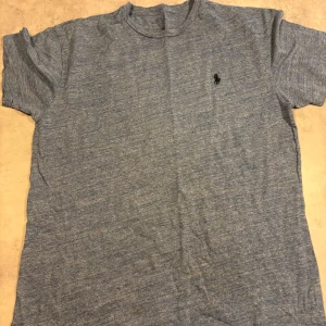 Blå t-shirt från Polo Ralph Lauren - Snygg blåmelerad t-shirt från Polo Ralph Lauren med klassisk broderad logga på bröstet. T-shirten har rund hals och korta ärmar, tillverkad i mjuk bomull som känns skön mot huden. Perfekt för dig som gillar stilrena och enkla plagg.