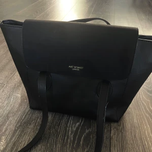 Svart axelväska från Art Street London - Stilren svart axelväska i skinnimitation från Art Street London. Väskan har långa handtag, magnetlås och ett rymligt huvudfack med innerfickor. 