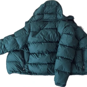 Grön dunjacka från Polo Ralph Lauren - Snygg mörkgrön dunjacka från Polo Ralph Lauren med puffig passform och dragkedja framtill. Jackan har huva och två sidofickor med dragkedja. Perfekt för kalla dagar när du vill hålla stilen och samtidigt vara varm.