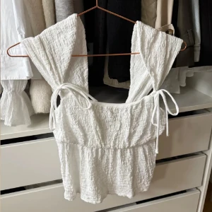 Vit topp - Superfin vit linnetopp med breda axelband och knytband på axlarna. Toppen har en strukturerad, lite skrynklig yta och fyrkantig ringning!