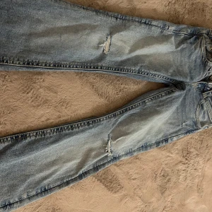 Ljusblå jeans från Gina Tricot, strl 140 - Snygga ljusblå jeans från Gina Tricot i storlek 140. Jeansen har slitna detaljer på benen, klassisk femficksmodell och raka ben. De är tillverkade i bomull och har coola bakfickor med knapp. Perfekta för en avslappnad och trendig look.