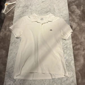 Vit piké från C.P. Company - Vit pikétröja från C.P company. Tröjan har en liten broderad logga på bröstet och knäppning vid halsen. Tillverkad i mjuk bomull som känns skön mot huden. Perfekt för en clean och stilren look. Den har storlek S och har väldigt fin kvalitet. Nypris är runt 1300, mitt pris är 449. Priset är diskuterbart fråga vid minsta fråga!
