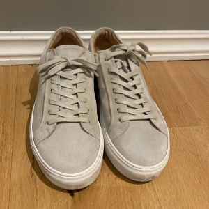 Ljusgrå mockasneakers med snörning - Stilrena sneakers i ljusgrå mocka med klassisk rund tå och vit platt sula. Skorna har snörning framtill och en minimalistisk design som passar till det mesta. Insidan är fodrad i beige och sulan har bra grepp. Obetydligt använda!