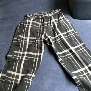 Svarta rutiga byxor från Björn Borg - Snygga svarta byxor från Björn Borg med vitt rutmönster och elastisk midja med logotyp. Perfekta för chill dagar hemma eller när du vill ha en avslappnad stil. Mjukt material som känns skönt mot huden.