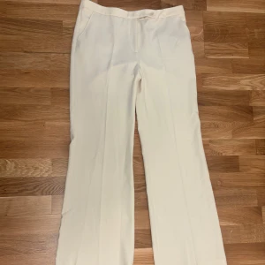 Beiga kostymbyxor från Zara L - Stilrena beiga kostymbyxor från Zara i storlek L. Byxorna har raka ben, hög midja och klassisk knappstängning framtill. Perfekta för en clean och dressad look. Materialet känns mjukt och har en lätt struktur.