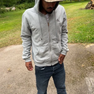 Grå hoodie från Burberry med dragkedja - Säljer en stilren ljusgrå hoodie från Burberry med dragkedja framtill, huva med snörning och två stora fickor. Perfekt för dig som gillar klassisk streetstyle och vill ha något bekvämt och snyggt. Passar både till jeans och joggers. Behöver sälja den då jag är behov av pengar. 