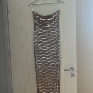 Glittrig långklänning från Bella Barnett - Säljer en beige långklänning från Bella Barnett med glittriga rektangulära paljetter över hela klänningen. Klänningen har en figurnära passform och är axelbandslös med dragkedja i ryggen. Perfekt för dig som vill sticka ut med en unik och glamorös look. Pris går att diskutera 