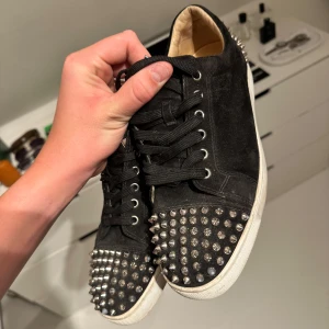Svarta mockasneakers med nitar(loubs) - Svarta sneakers i mocka med coola silvriga nitar över tå och häl. Skorna har svarta snören, vit sula och rund tå. Insidan är ljusbeige och materialet känns lyxigt. Perfekta för dig som vill sticka ut med en edgy vibe.