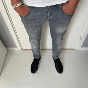 Dondup Jeans  - Snygga grå skinny jeans från dondup med coola slitningar och färgstänk för en trendig look. Jeansen har klassisk femficksdesign och smal passform som sitter tajt längs benen. Perfekta för dig som gillar streetstyle och vill sticka ut lite extra.