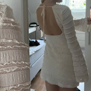 Klänning med öppen rygg - Supersöt ljusbeige kortklänning med långärmade armar och öppen rygg med knyt. Klänningen har ett strukturerat tyg med horisontella volangdetaljer som ger en unik look💛