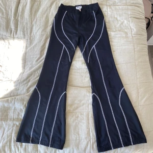 Svarta bootcut byxor från Madlady - Svarta bootcut byxor från Madlady med kontrasterande vita sömmar i coolt mönster. Byxorna har hög midja och är gjorda i stretchig polyester som sitter snyggt och bekvämt. Perfekta för dig som vill sticka ut med en trendig look.