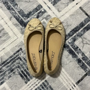 Beige ballerinaskor med rosett från Esmara - Söta beige ballerinaskor från Esmara med blommigt mönster och dekorativ rosett framtill. Skorna har rund tå och platt sula, perfekta för en stilren och feminin look.