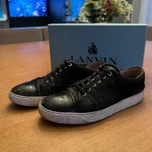 Svarta sneakers från Lanvin - Lanvin sneakers i svart mocka med lackad tå och vit platt sula. Klassisk låg modell med snörning och metallöglor. Snygg kontrast mellan material och färg, perfekt för dig som gillar stilrena och exklusiva sneakers, säljes i använt skick, se på bilder. Box medföljer. Bara att höra av sig vid frågor/prisförslag