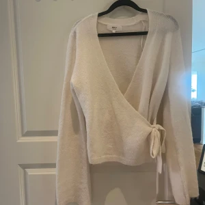 Beige omlottkofta från Gina Tricot - Supermjuk beige omlottkofta från Gina Tricot i ullblandning. Koftan har lång ärm, v-ringning och knyt i sidan för en snygg och avslappnad look. Perfekt att slänga på sig när det är lite kyligt ute.
