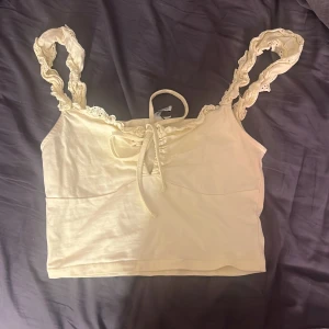 ljusgul linnetopp med spets från NLY Trend - Supersöt ljusgul linnetopp från NLY Trend med breda axelband i spets och en söt knytning framtill. Toppen är croppad och har romantiska detaljer som ger en feminin vibe. Perfekt att styla med jeans eller kjol för en trendig look.