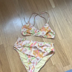 Blommig bikini i pastellfärger XS pris kan diskuteras  - Superfin bikini i storlek XS med blommigt mönster i pastelliga färger som gul, rosa, grön och vit. Använd 2 gånger ! Överdelen har smala axelband som korsas i ryggen och knäpps med spänne. Materialet är mjukt och stretchigt i 84% polyester och 16% elastan. Perfekt för sommaren! Storleken i toppen är xs/ 70A. Man kan även lägga i vaddering i toppen!