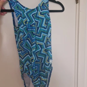 Blå mönstrad gymnastikdräkt - Snygg gymnastikdräkt med coolt geometriskt mönster i blå, grön och gul. Modellen har klassisk rund hals och ärmarna är skurna för att ge en sportig look. 