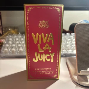 Juicy Couture Viva La Juicy parfym 50ml - Juicy Couture Viva La Juicy parfym i en lyxig glasflaska med guldiga detaljer, stor kristallformad kork och röd rosett. Flaskan har en guldig Juicy Couture-logga och hängsmycke. Kommer i en rosa och guldig kartong. 50 ml Eau de Parfum. Den är helt ny och har enbart sprayat ett sprut för att lukta på den.