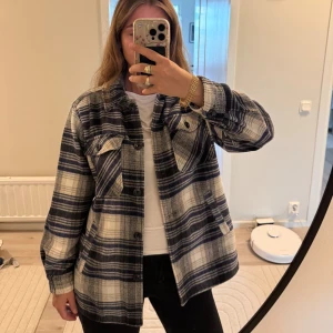 Höst kappa/jack - Säljer en riktigt snygg overshirt med rutigt mönster i blått och vitt. Jackan har knappar framtill, två bröstfickor med lock och långa ärmar med knapp vid mudden. Perfekt att slänga över en t-shirt för en chill look.
