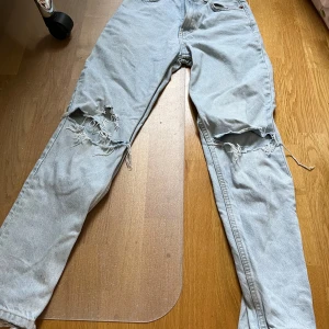 Ljusblå ripped jeans från Zara - Säljer ett par ljusblå jeans från Zara med raka ben och stora slitningar över båda knäna. Klassisk femficksmodell i denim med normal passform. Perfekta för en avslappnad och trendig look.
