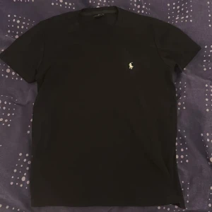 Svart Ralph Lauren T-shirt - Klassisk svart t-shirt från Ralph Lauren med liten broderad logga på bröstet. T-shirten har rund halsringning och korta ärmar. Perfekt basplagg med stilren design.
