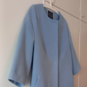 Ljusblå kappa från Finn Flare - Säljer en stilren ljusblå kappa från Finn Flare i storlek XL. Kappan har trekvartsärmar, dold knäppning och ett vackert blommigt foder på insidan. Perfekt för vår och höst när du vill ha en klassisk look.   NY pris1399:-