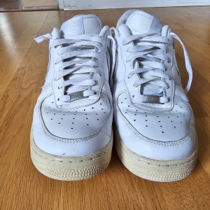 Vita Nike Air Force 1 sneakers  - Klassiska vita Nike Air Force 1  med lågt skaft och rund tå. Skorna har snörning och är tillverkade i skinn med en platt sula. Det finns små defekter men de påverkar varken funktionalitet eller estetik. Se de sista 2 bilderna. Skorna är i använt skick, därav priset.