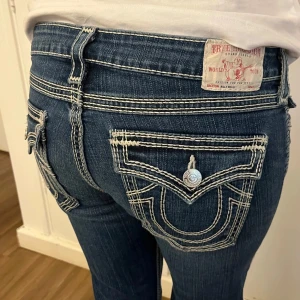 True Religion jeans - Snygga blåa jeans från True Religion med vit sömn Jeansen har en avslappnad stil och är raka nedtill 💘Storlek 32 i midjan och innerbenslängden är ca 28 (71 cm)! Midjemåttet tvärs över är ca 44 cm💘💖
