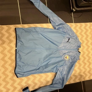 Manchester City vindjacka  - Ljusblå vindjacka från Puma med Manchester City. Aldrig använd då den är förstor.