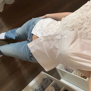 Vit blus med spetsdetaljer och rosett i ryggen - Säljer en vit blus med vackra spetsdetaljer framtill och korta ärmar. Blusen har en feminin passform och knäppning framtill. Perfekt att styla med jeans för en fräsch look.