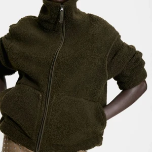 Olivgrön teddyjacka med dragkedja - Mysig olivgrön teddyjacka med hög krage och dragkedja framtill. Jackan har långa ärmar och två praktiska fickor. Perfekt för kyliga dagar. Prislapp kvar då jag ångrat mig 😊 kostar 200