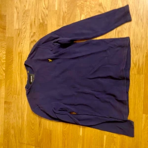 Mörkblå långärmad tröja från Morris - Säljer en stilren mörkblå långärmad tröja från Morris med liten gul broderad logga på bröstet. Perfekt för en enkel och klassisk look. Tröjan har rund hals och är i ett mjukt material.