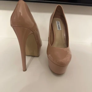 Beiga platåpumps från Steve Madden - Säljer ett par snygga beiga pumps från Steve Madden med hög klack och platåsula. Skorna har rund tå och är tillverkade i glansig syntet. Perfekta för dig som vill ha extra höjd och stil.