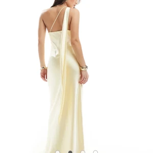 Gul långklänning med scarf - Säljer en oanvänd gul (citron färgad) långklänning i glansig satin. Klänningen har oneshoulder-design med en lång draperad detalj på axeln och en smickrande, figurnära passform. Perfekt för speciella tillfällen. Prislappen sitter kvar