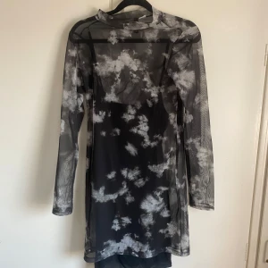 Svart och vit meshklänning med molnmönster - Säljer en svart meshklänning med vita molnliknande mönster. Klänningen har lång ärm, hög hals och är genomskinlig med en tight passform. Perfekt för att styla lager på lager eller med ett linne under.