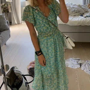 Blommig klänning från Stradivarius - Säljer en superfin blommig klänning från Stradivarius i storlek S. Den har en v-ringad design med korta ärmar och ett elastiskt band i midjan för en bekväm passform. Klänningen är i ett lätt och luftigt material med ett härligt blommönster i blått och grönt. nypris är 460kr