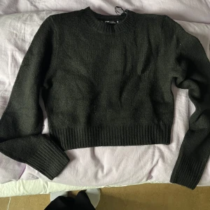 Svart croppad stickad tröja - Mysig svart croppad stickad tröja med rund halsringning och breda ribbade muddar vid ärmslut och nederkant. Perfekt för lager-på-lager och enkel att matcha med olika outfits.